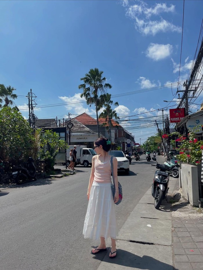 Sambil menikmati pemandangan, ia asyik menjelajahi berbagai tempat, salah satunya mengunjungi Asmara Butik. Outfit-nya yang sederhana dengan tank top pink, rok putih, dan sandal semakin memancarkan nuansa tropis./ Foto: instagram.com/j_chaeyeoni