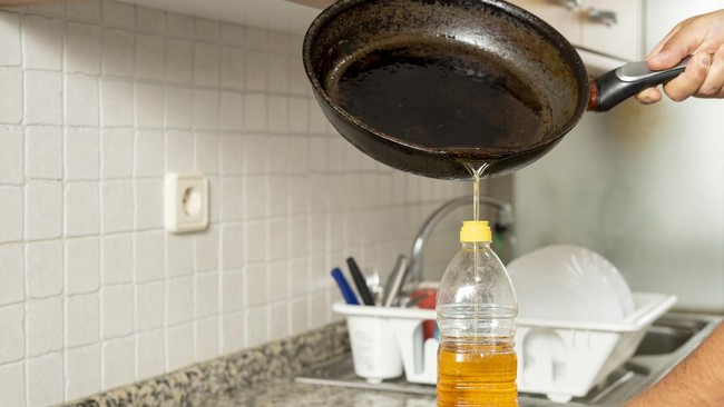 Man placing recycled edible oil from a frying pan into a plastic bottle in his home kitchen. Recycle at home concept