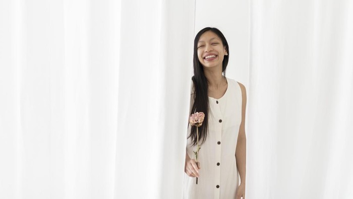 Happy Asian woman with a dry pink peony flower in a hand among the white curtain