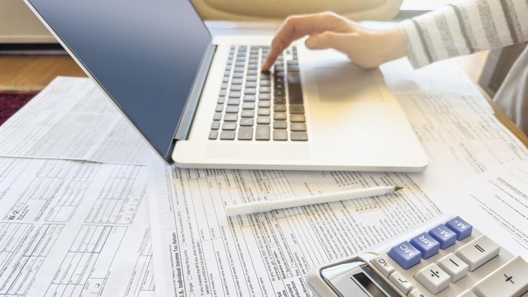 Ilustrasi pajak penghasilan Close up photo of a woman doing taxes with laptop and tax forms in a house