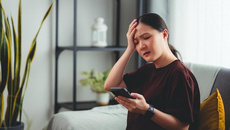 Asian pregnant woman using smartphone feeling stressed and negative emotion, sitting in living room at home.