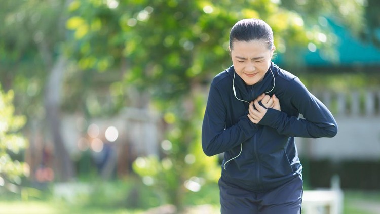 Ilustrasi nyeri dada saat olahraga Portrait of Asian woman wearing earphones listening to music was sick with chest pain at park. Woman exercise at park suffering from painful chest.