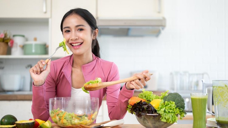 Ilustrasi diet An attractive and cheerful Asian woman in sportswear enjoys her healthy salad at a kitchen table in the kitchen. Healthy lifestyle concept