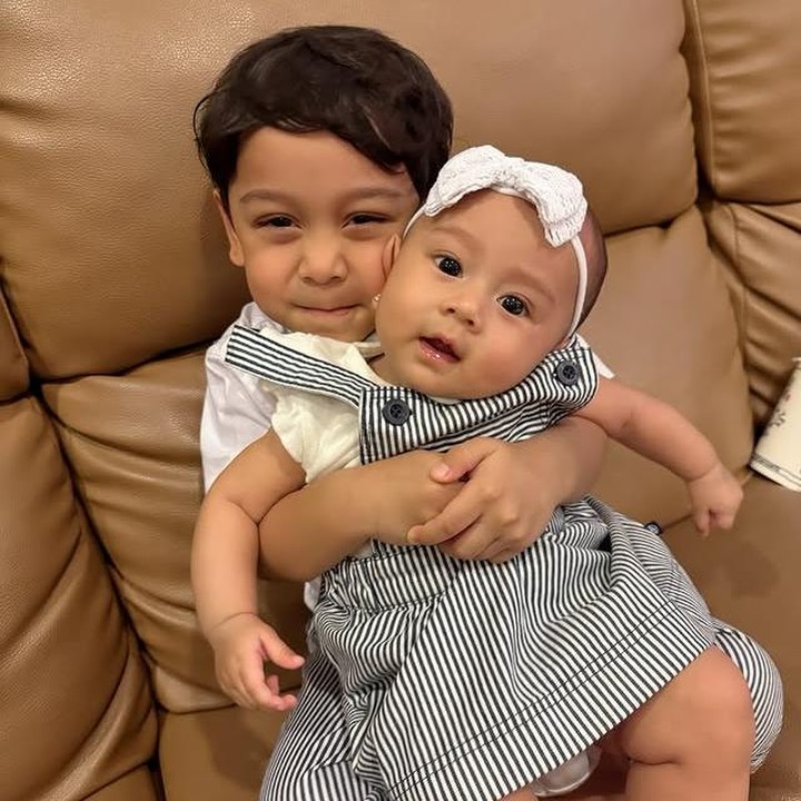 <p>Tak cuma sekali, Levian kembali menunjukkan kasih sayangnya dengan memeluk erat sang adik. Meski badannya kecil, Levian terlihat sudah sangat lihai memangku Leshia, yang juga tampil lucu memakai <em>dress</em> dan bandana berwarna putih. (Foto: Instagram @leshiativana)</p>