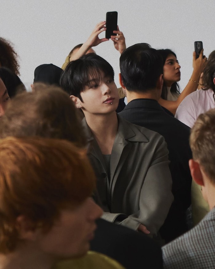 Jungkook BTS hadiri fashion show Calvin Klein SS26. Ia mengenakan busana Calvin Klein berupa setelan jas abu-abu.