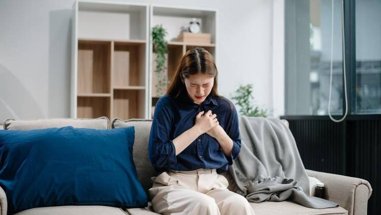 Young Asian woman suffering from flu symptoms, covered with a blanket on a sofa. Concept of illness, healthcare, and recovery. Stay indoors, stay healthy