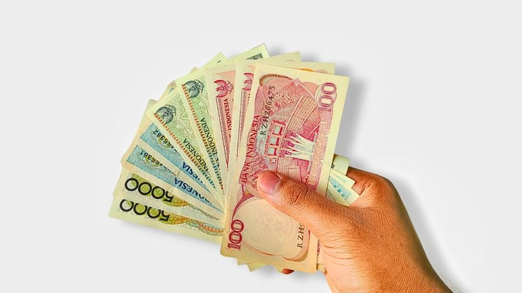 hand holding old vintage Indonesian currency denominations of 5,000 rupiah, 1,000 rupiah, and 100 rupiah on a clean white background