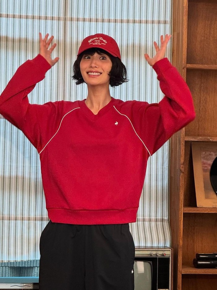 Nana tampil mencolok dengan kaus merah yang senada dengan topinya. Ia menambahkan celana training hitam yang kontras untuk tampilan sporty yang sempurna.