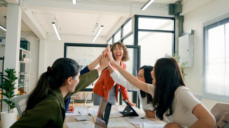 A diverse team of business professionals celebrating with a high-five during an ESG (Environmental, Social, and Governance) meeting in a bright, modern office environment.