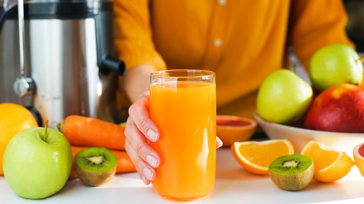 Ilustrasi buah potong dan jus A woman's hand holds a glass of freshly made natural multifruit juice. Healthy and tasty juices at home. Using a juicer. Close-up. Selective focus.