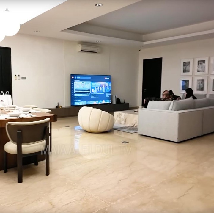 <p>Mengusung open space, ruang keluarga mereka menampilkan sofa abu-abu muda yang panjang untuk bersantai. Di depannya, televisi layar lebar menempel di dinding, ditemani AC split dan plafon bertingkat yang menambah kesejukan. Dinding sebelah kanan dihiasi foto hitam-putih pernikahan Alyssa dan Al, sementara ruang makan menyatu dengan area keluarga. (Foto: Youtube @maiaaleldultv)</p>