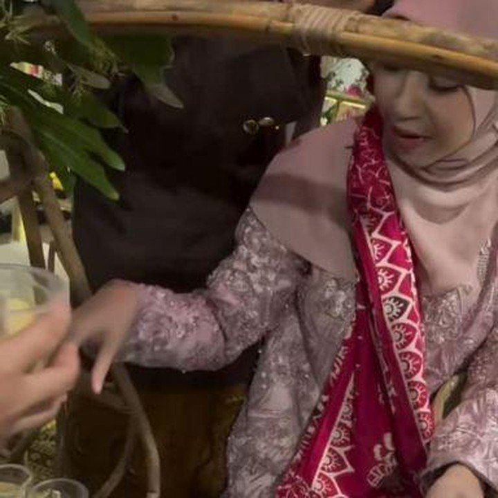 <p>Di acara tasyakuran ini, Adiba dan Egy juga menjaani prosesi berjualan cendol. Sambil mengenakan baju berwarna merah muda, Adiba terlihat sangat luwes memeragakan proses berjualan cendol. Sementara itu, Egy tampak memayungi istrinya yang sedang sibuk berjualan. (Foto: Instagram @_ummi_pipik_/ @adiba.knza)</p>