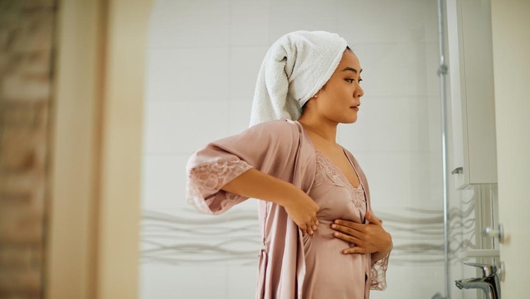 ilustrasi payudara Young Asian woman standing in front of bathroom mirror while doing breast self-examination. Copy space.