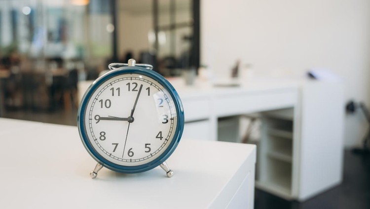A blue alarm clock sits on a white desk in a room.