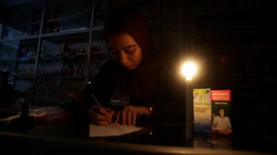 Seorang pedagang mencatat daftar obat-obatan menggunakan bantuan penerangan lilin saat terjadi pemadaman listrik di Pasar Keutapang, Kabupaten Aceh Besar, Aceh, Rabu (1/10/2025). PLN Unit Induk Wilaya