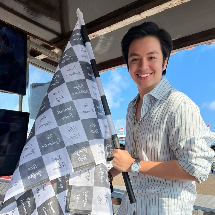 <p>Di ajang MotoGP kali ini, Angga berkesempatan untuk mengibarkan bendera finis di pinggir sirkuit. Ketika melaksanakan tugasnya, Angga terlihat santai mengenakan kemeja bergaris putih hitam yang dipadukan dengan celana putih. (Foto: Instagram @angga/ @sheninacinnamon)</p>