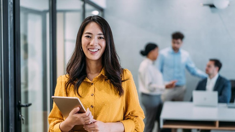 Shot of a beautiful smiling businesswoman standing in front of her team and holding digital tablet. Portrait of successful businesswoman standing with her colleagues working in background.