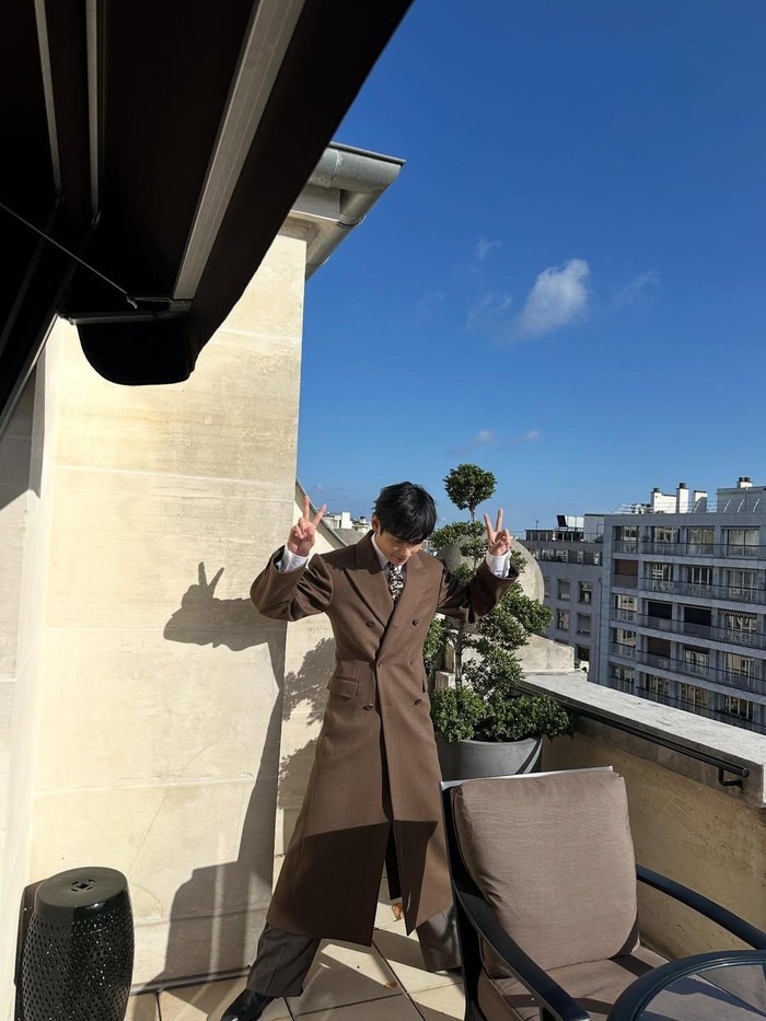 Look V BTS di PFW25 juga tidak kalah memukau lho, Beauties! Ya, ia tampil menawan bak bangsawan berbalut mantel double-breasted coklat dipadukan dengan celana panjang loose fit serta kemeja putih dengan dasi bermotif./ Foto: instagram.com/thv