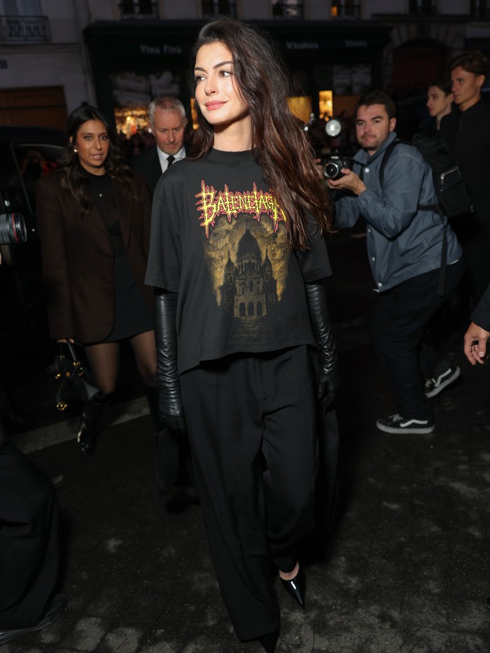 Anne Hathaway tampil awet muda dalam balutan outfit custom terdiri dari graphic tee dengan jubah serta wide leg pants. All-black look ini makin stunning dengan padu padan opera gloves dan pointy shoes/ Foto: Courtesy of Balenciaga/Getty Images for Balenciaga/Arnold Jerocki