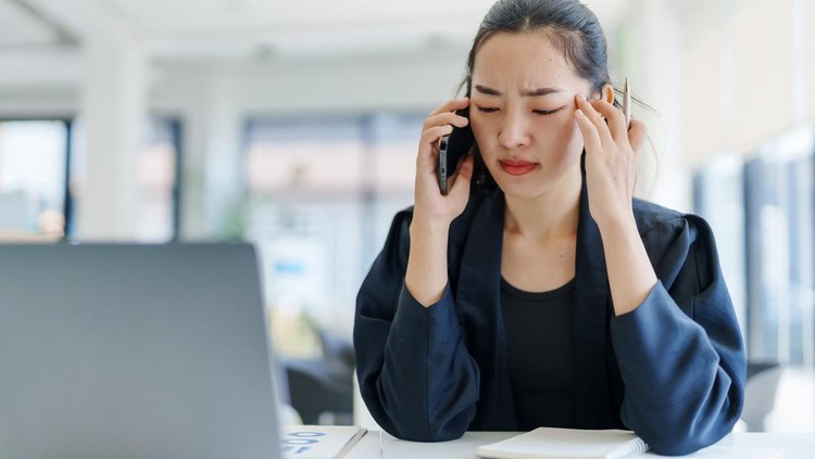 Ilustrasi perempuan di kantor Young Asian businesswoman having a headache and massaging her temples while making a phone call in the office