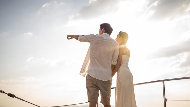 Ilustrasi trophy wife Asian young romantic couple looking at beautiful view during yachting. Attractive man and woman hanging out celebrating anniversary honeymoon trip while catamaran boat sailing during summer sunset.
