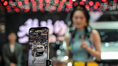 A social media influencer does streaming next to a car during the 21st Shanghai International Automobile Industry Exhibition at the National Exhibition and Convention Center in Shanghai on April 24, 2