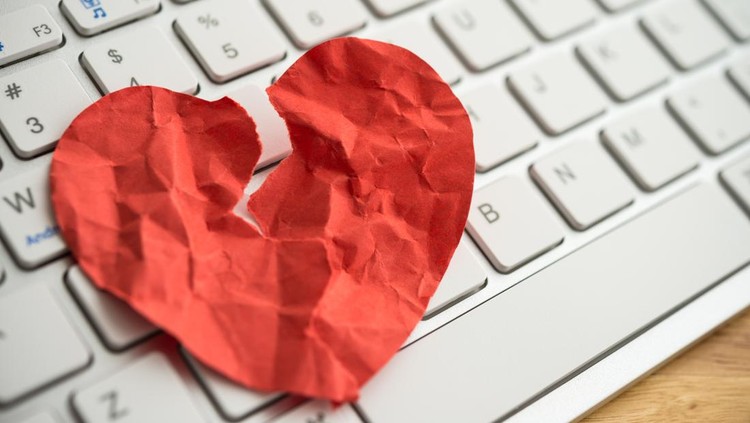 Red broken heart paper on white keyboard computer background. Online internet romance scam or swindler in website application dating concept. Love is bait or victim.