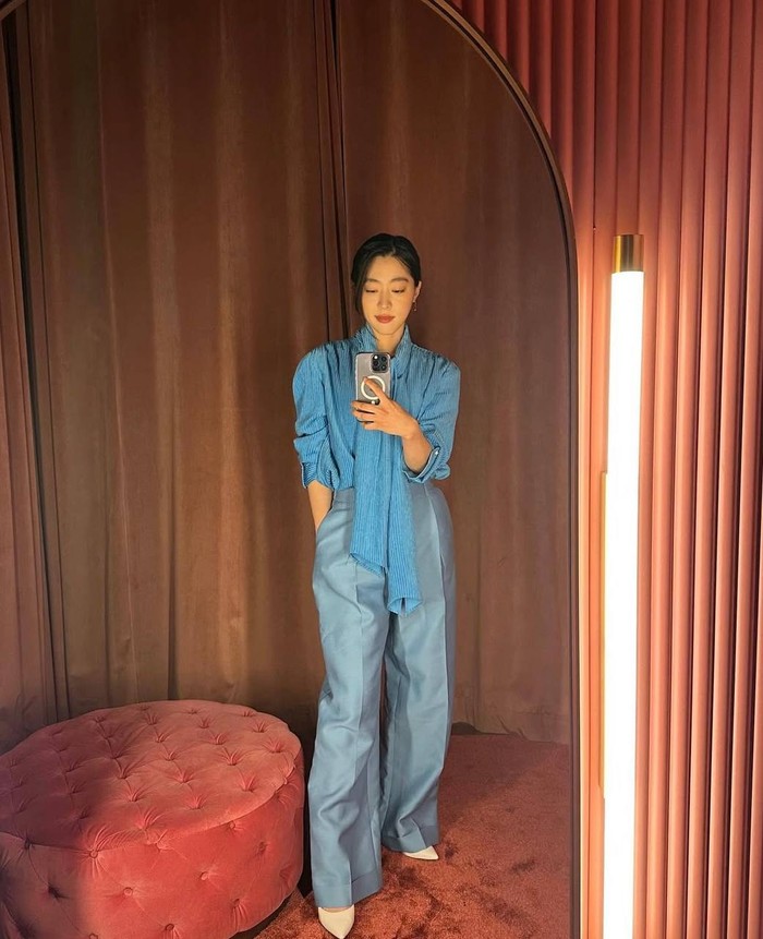 Ia menggunakan outfit bernuansa biru dengan blouse kemeja dengan detail scarf di leher dan celana wide leg sedikit mengilap serta sepatu heels putih gading yang bikin look-nya terlihat rapi dan classy./ Foto: Instagram.com/choisungeun.official