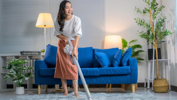 Young woman happily vacuuming the carpet in a cozy living room, surrounded by comfortable furniture and decorative plants