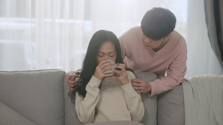 A warm and caring moment captured as a young man tenderly offers a cup of coffee to his partner, enhancing their cozy morning at home.