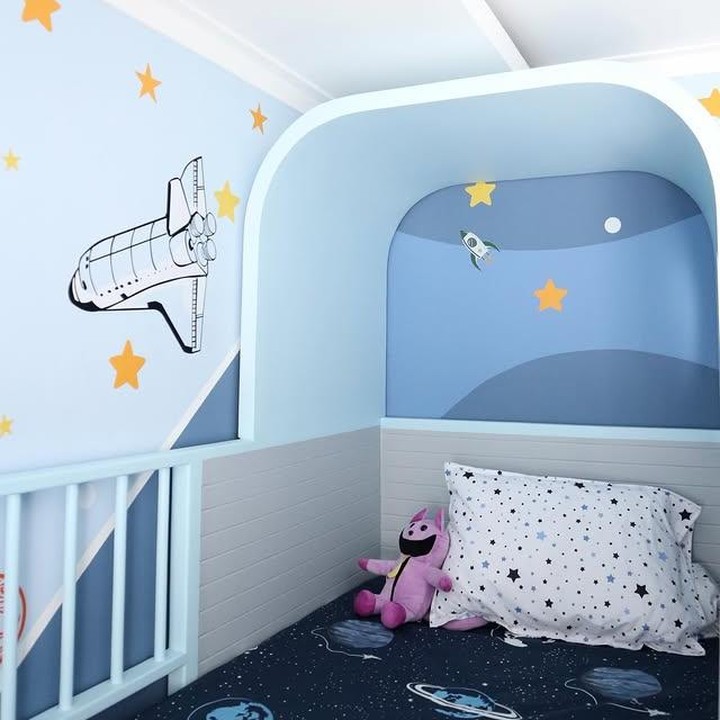 <p>Jika dilihat dari bagian depan kasurnya, dinding kamarnya tampak dihiasi mural&nbsp;Space Shuttle dan bintang yang cantik. Kasurnya pun dibuat luas, lengkap dengan sprei yang juga bertema luar angkasa, Bunda. (Foto: Instagram @melodyprima)</p>