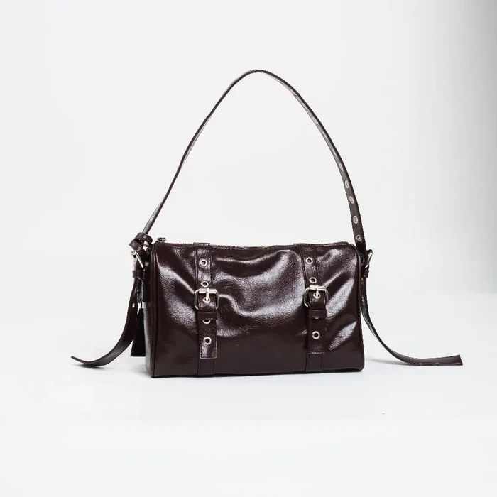 Katniss bag dari brand CHEKAS memiliki siluet persegi panjang dengan material dari kulit sintetis berwarna coklat tua dengan finishing glossy. Ada aksen buckle atau gesper yang cukup mencolok di bagian depan.