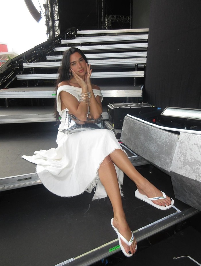 Dua Lipa mix-and-match dress putih dengan sandal jepit. Ia berikan penghormatan untuk Brasil dengan memakai Haiavainas Brasil Logo.