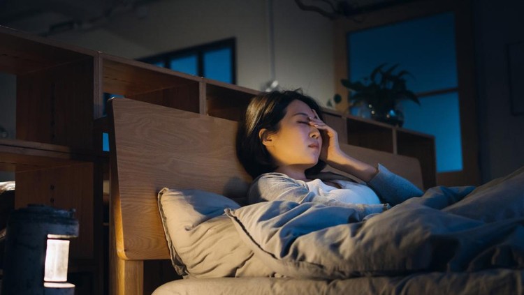 Young Asian woman feeling sick and suffering from a headache, lying on bed and taking a rest at home