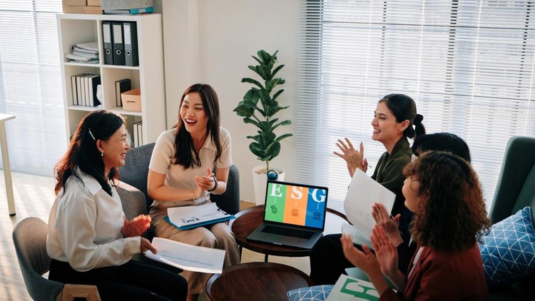 A group of professional women enthusiastically high-five in a bright modern office, celebrating a shared achievement during an ESG (Environmental, Social, Governance) meeting.