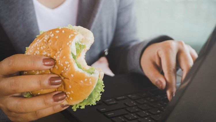 business woman eating junk food burger while working on computer laptop, unhealthy lifestyle concept