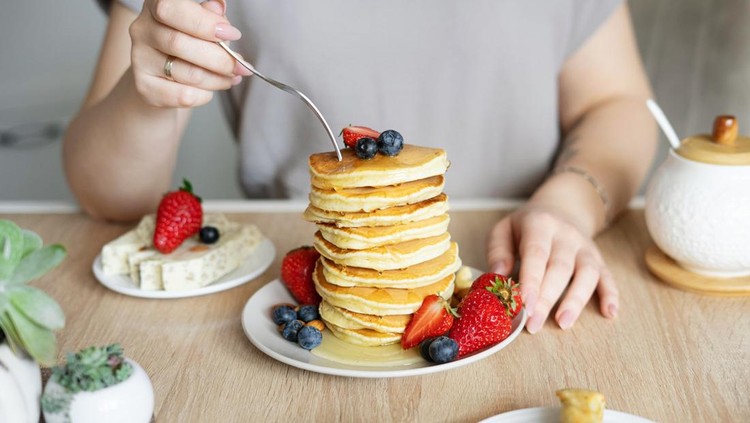 A woman eats pancakes garnished with strawberries and blueberries with a fork. Beautiful breakfast close-up.
