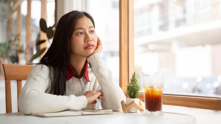 An asian woman is putting her hand under the chin&comma; looking bored or unhappy while waiting for someone at the round marble table&period; Study or Working in the cafe&period;