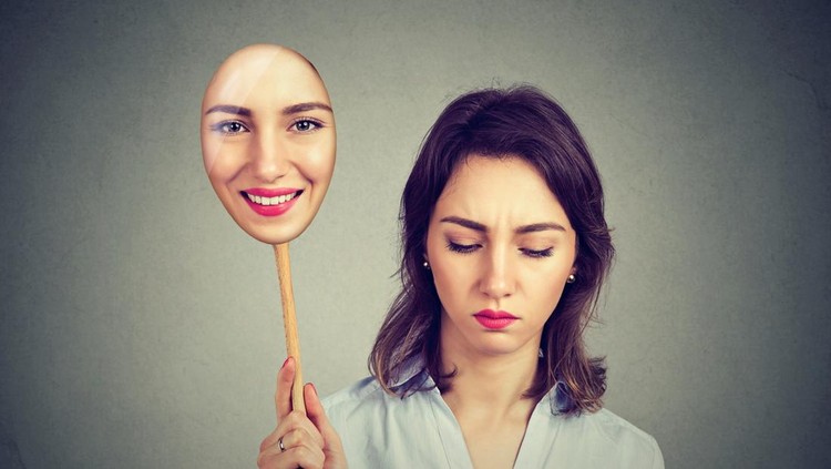 Sad woman looking down taking off happy mask of herself