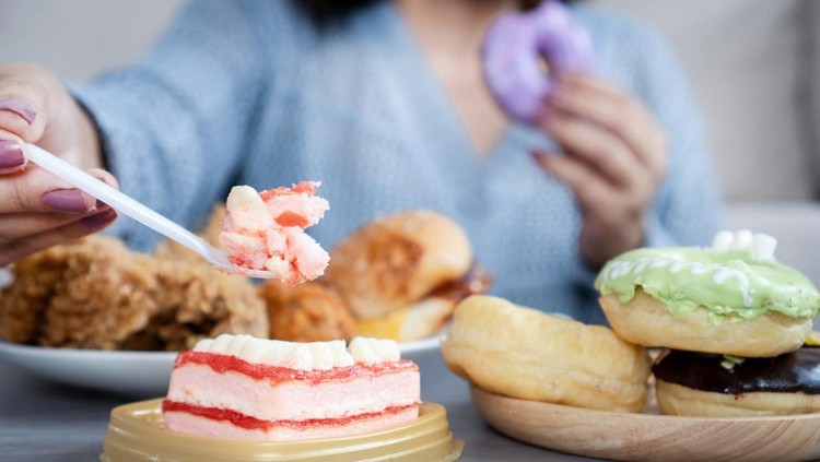 Woman eating too much fast food like burgers&comma; fried chicken&comma; donuts&comma; and sweets&comma; showing signs of binge eating and emotional stress with unhealthy food habits