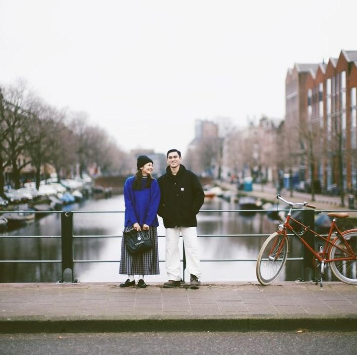 <p>Melalui unggahan di Instagram, Enzy membagikan potretnya bersama sang suami saat berada di Amsterdam, Bunda. Perempuan 33 tahun ini berpose bersama suami dengan latar pemandangan sungai dan bangunan-bangunan khas di Belanda. Enzy menuliskan <em>caption</em> singkat, yakni emoji hati biru muda yang dapat melambangkan rasa cinta, kehangatan, dan kebahagiaan. (Foto: Instagram @enzystoria)</p>