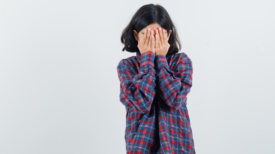 young girl covering face with hand in checked shirt and looking timid&period; front view&period;