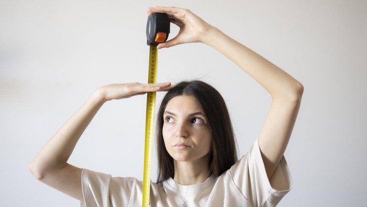Young girl Checking Her Height With a Yellow Measuring Tape Indoors