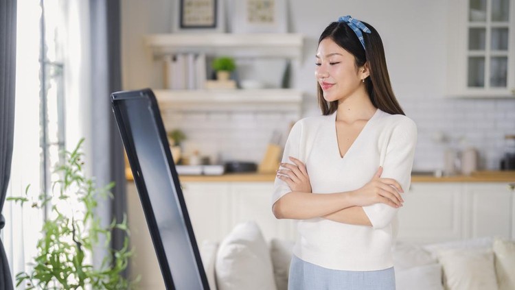 A confident&comma; cheerful Asian woman smiles warmly as she looks at herself in the mirror at home&comma; embracing self-love&comma; inner strength&comma; and positivity through daily self-care and personal empowerment&period;