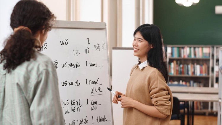 Portrait of friendly Asian woman teaching Chinese language to student standing by whiteboard in class
