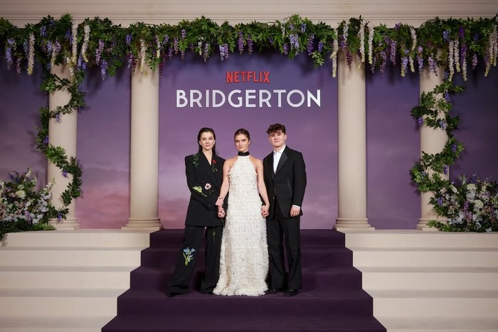 Siapa sih yang nggak suka melihat tiga Bridgerton bersaudara ini? Claudia Jessie mengenakan setelan jas berbordir bunga karya Stella McCartney, kontras dengan Florence Hunt yang feminin dengan gaun putih halter neck yang dipenuhi detail kelopak bunga rancangan Dior. Sementara itu, Will Tilston tampil klasik dengan setelan jas dengan kemeja putih/ Foto: instagram.com/bridgertonnetflix