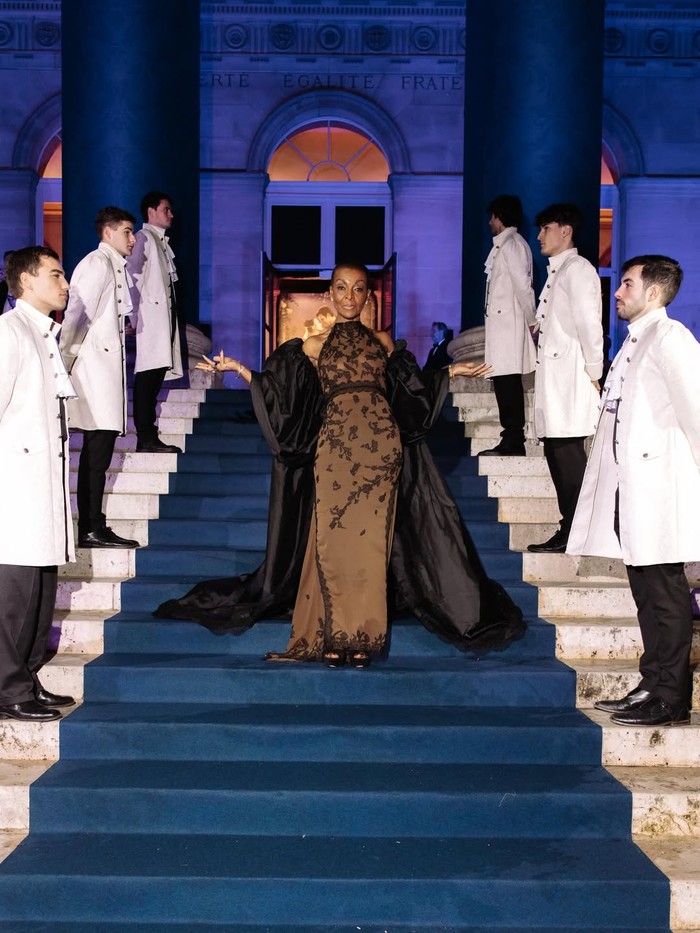 Adjoa Andoh, pemeran Lady Dunbury, pancarkan pesona 'Regencycore' modern melalui gaun rancangan Torlowei. Siluet halter neck berpadu kerah tinggi, rona coklat dengan detail renda hitam, ditambah drama dengan jubah yang senada/ Foto: instagram.com/bridgertonnetflix