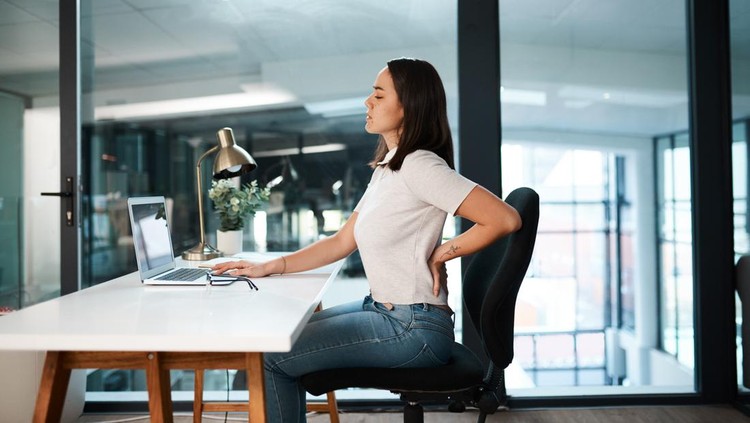 Shot of a young businesswoman experiencing back pain while working in an office