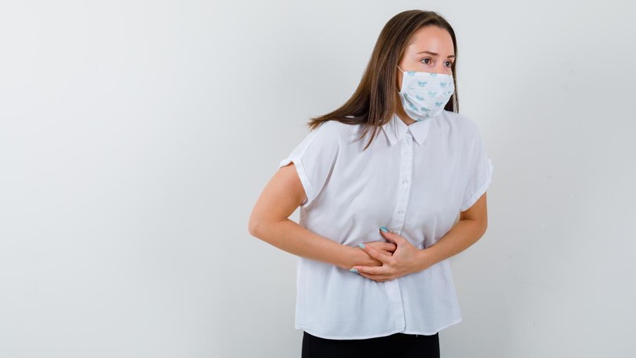 pretty lady suffering from stomach pain in t-shirt&comma; mask and looking painful &comma; front view&period;