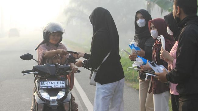 Sejumlah mahasiswa yang tergabung dalam Ikatan Pemuda Pelajar Mahasiswa Samatiga (IPMS) membagikan masker kepada pengendara yang melintas di jalan lintas Nasional Medan-Banda Aceh Desa Suak Nie, Johan Pahlawan, Aceh Barat, Aceh, Sabtu (24/1/2026). Pe